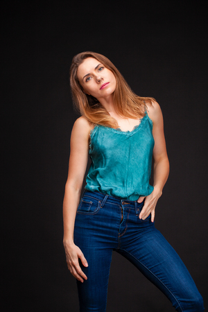 Fashion shoot of young sexy woman in blue jeans and green blouse in dark studioの写真素材