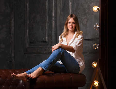 Fashion shoot of young sexy woman in blue jeans and white shirt in dark studioの写真素材