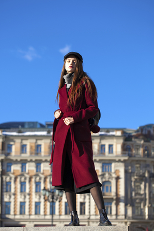 Full body portrait. Young beautiful brunette woman in stylish in a long burgundy coat walking in spring streetの写真素材