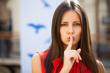 Woman requires silence. Young beautiful brunette girl has put forefinger to lips as sign of silence, isolated on white backgroundの写真素材