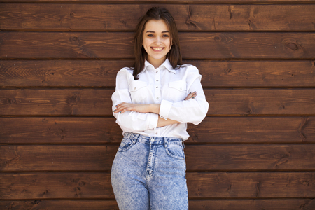 Portrait of a teenager girl in a white shirt on a wooden wall backgroundの写真素材