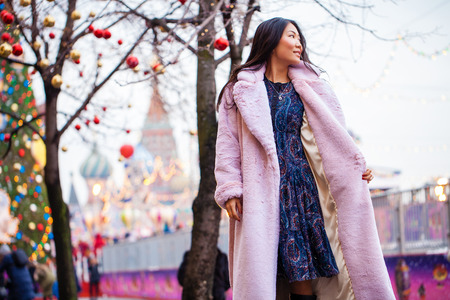 Happy asian woman in winter coat from faux fur, walking on red square, Russiaの写真素材
