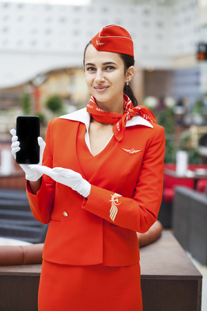 RUSSIA, MOSCOW: 28 JUNE 2019. Beautiful stewardess dressed in official red uniform of Aeroflot Airlines on airport. Young woman with mobile phoneのeditorial素材