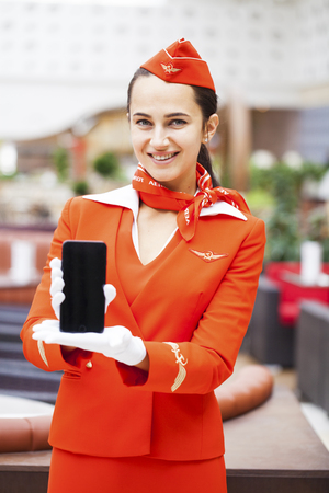 RUSSIA, MOSCOW: 28 JUNE 2019. Beautiful stewardess dressed in official red uniform of Aeroflot Airlines on airport. Young woman with mobile phoneのeditorial素材