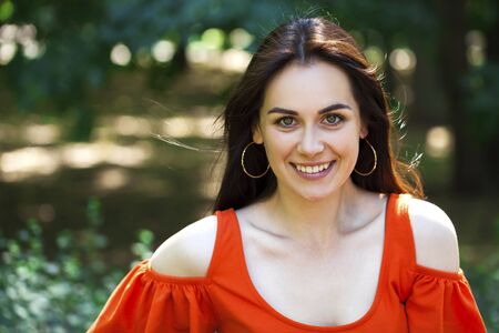 Portrait close up of young beautiful brunette woman in red dress, summer street