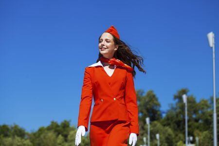 Close up portrait woman. Beautiful stewardess dressed in official red uniform gainst a blue skyの写真素材