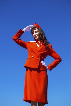 Close up portrait woman. Beautiful stewardess dressed in official red uniform gainst a blue skyの写真素材