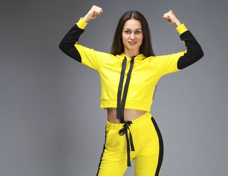 Portrait of a young beautiful brunette woman in yellow tracksuit, isolated on gray backgroundの写真素材