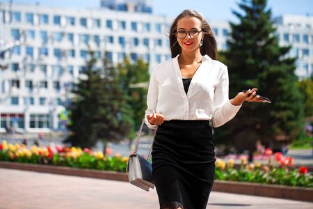 Young happy brunette woman in black skirt and blouse walking in the summer streetの写真素材