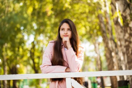 Portrait of a young beautiful brunette girl in pink coat on a background of autumn parkの写真素材