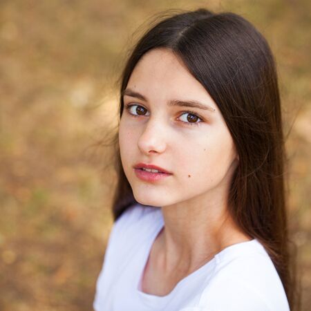 Portrait of a young beautiful brunette girl in white t-shirt on a background of a summer park
