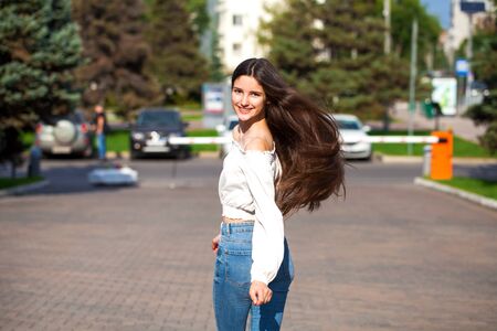 Portrait of young beautiful brunette woman in jeans and white blouse walking in summer streetの写真素材