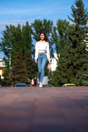 Full body young model. Portrait of young beautiful brunette woman in jeans and white blouse walking in summer streetの写真素材