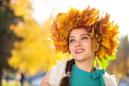 Close up portrait of a young beautiful woman with a wreath of maple leaves posing in autumn parkの写真素材