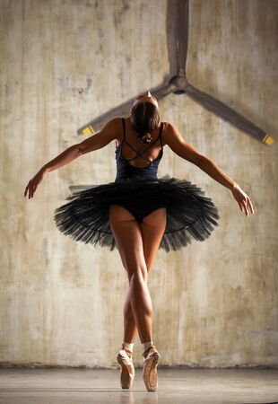 Full body portrait. Young ballerina in a black dancing suit is posing in dark studioの写真素材