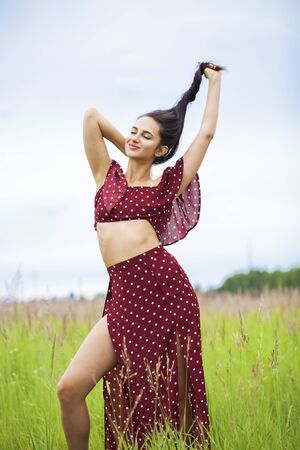 Full-length portrait of a young beautiful woman in a sexy dress posing against the background of a meadow fieldの写真素材