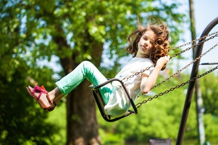 Happy Little girl on a swing in the summer park
