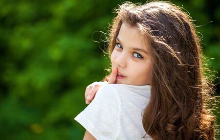 Young beautiful Little girl has put forefinger to lips as sign of silence, outdoors summer