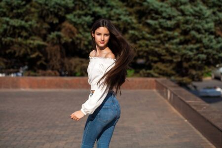 Portrait of young beautiful brunette woman in jeans and white blouse walking in summer streetの写真素材