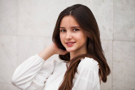 Closeup portrait of a young beautiful girl on a background of a white marble wall