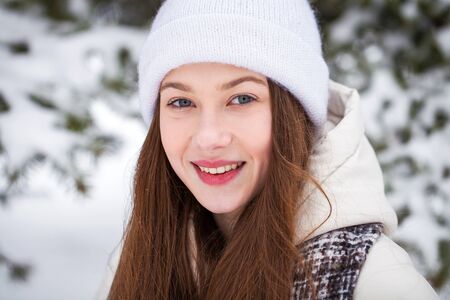 Close up portrait of a young beautiful girl in a white down jacket posing in a winter parkの写真素材