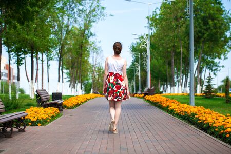 Full body portrait of a beautiful young brunette woman walking in flowers dress, summer park outdoorsの写真素材