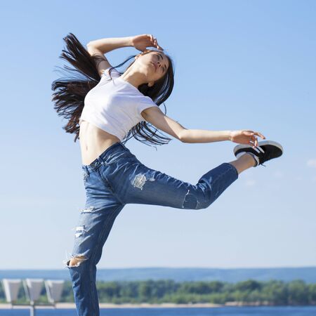 Full body girl in a jump. Young beautiful brunette woman posing against blue sky bright sunny...