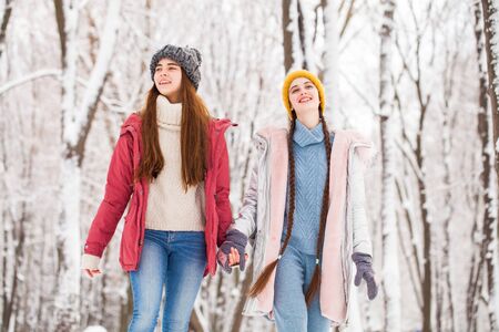 Two young beautiful girlfriends walk in the winter in a city parkの写真素材