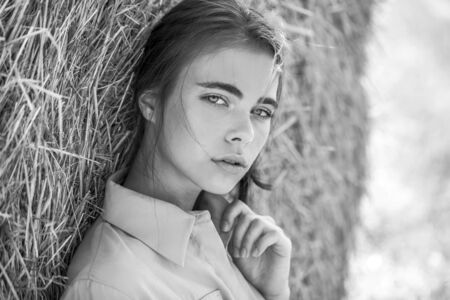 Beautiful calm girl posing on a background of haystacks in a cut field.