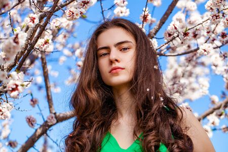 Pretty teen girl are posing in garden near blossom cherry tree with white flowers. Spring time