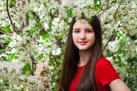 Pretty teen girl are posing in garden near blossom cherry tree with white flowers. Spring timeの写真素材
