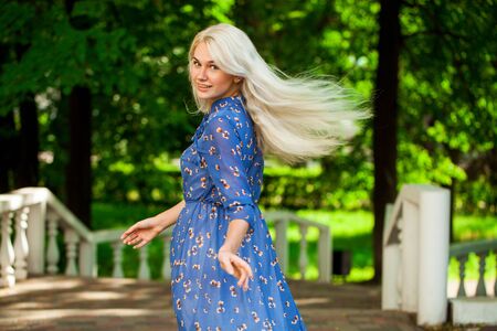 Portrait of a young beautiful blonde girl in blue flowers dress walking in summer parkの写真素材
