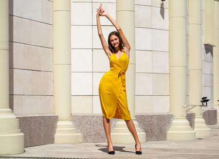 Young beautiful girl in a bright yellow coat sits on a carousel in an amusement parkの写真素材