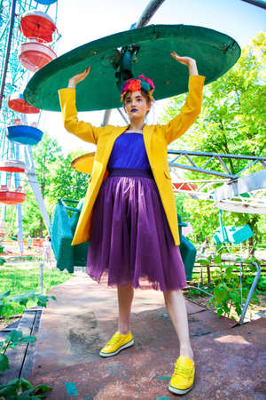 Portrait of a stylish model in a yellow coat posing against the backdrop of amusement park