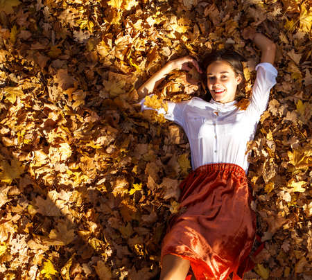 Full body portrait of a young brunette woman in orange skirt walking in autumn parkの写真素材