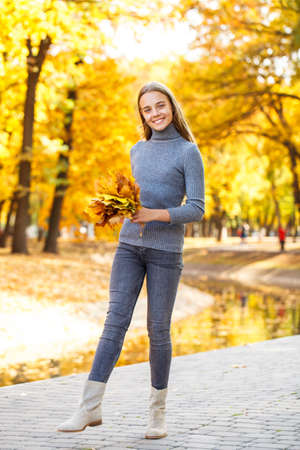 Â Full body portrait of a young beautiful blonde girl in white sweater and blue jeans, autumn park outdoorの写真素材