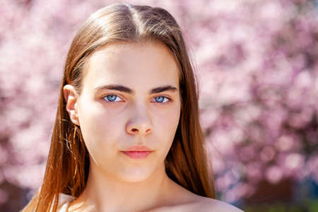 Pretty teen girl are posing in garden near blossom cherry tree with white flowers. Spring time