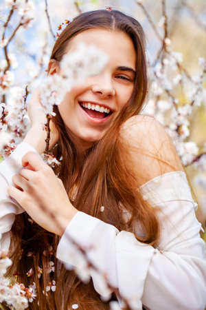 Pretty teen girl are posing in garden near blossom cherry tree with white flowers. Spring time