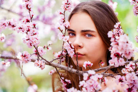 Pretty teen girl are posing in garden near blossom cherry tree with white flowers. Spring timeの写真素材
