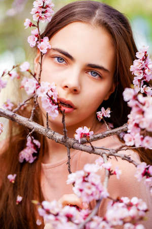 Pretty teen girl are posing in garden near blossom cherry tree with white flowers. Spring timeの写真素材