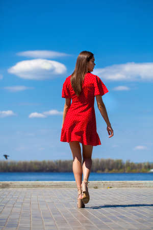 Portrait of a young beautiful girl in a short red dress posing on the embankmentの写真素材