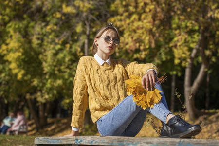 Full-length portrait of a young girl in a woolen sweater and torn jeans posing in an autumn parkの写真素材