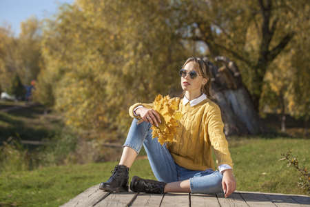 Full-length portrait of a young girl in a woolen sweater and torn jeans posing in an autumn parkの写真素材