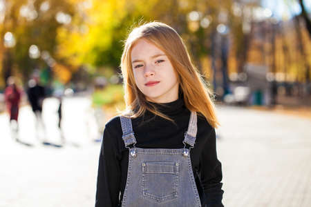 Portrait of a red-haired little girl in a black hat walks in the autumn parkの写真素材