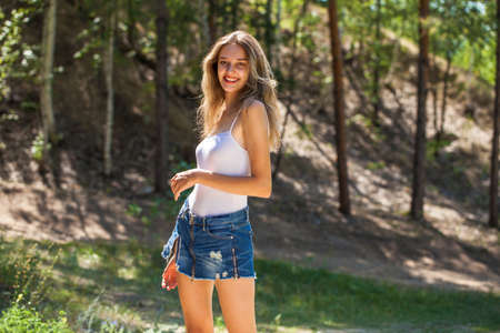 Full body portrait of a young beautiful blonde girl in blue jeans, summer park outdoors