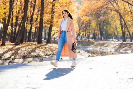 Full-length portrait of a young girl in blue jeans posing in an autumn park