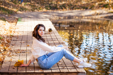 Full-length portrait of a young girl in blue jeans posing in an autumn parkの写真素材