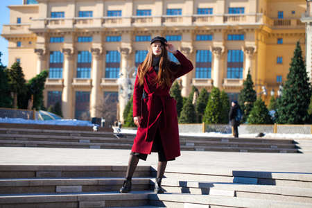 Full body portrait. Young beautiful brunette woman in stylish in a long burgundy coat walking in spring streetの写真素材