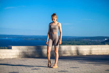 Young beautiful girl in sports uniform is engaged in fitness outdoors