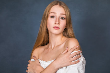 Close up portrait of a young beautiful blonde girl in white dress - isolated on blue backgroundの写真素材